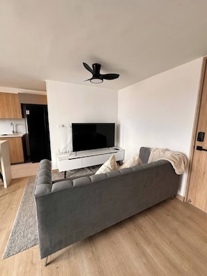 A modern living room with a grey sofa, a flat-screen TV, a ceiling fan, and a wooden floor. - Epic View 25 Pablo Tobón Cardiovascular (Medellín)