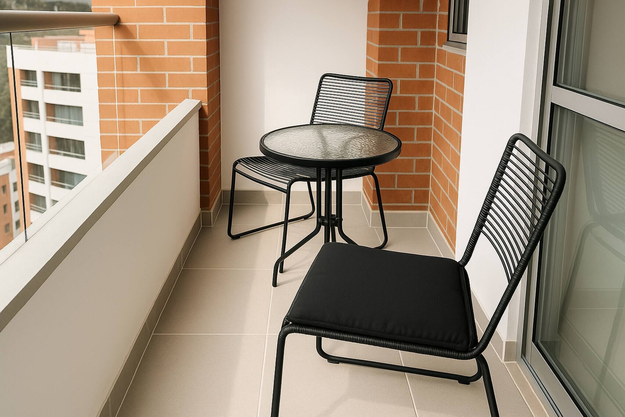 Ein Balkon mit rundem Tisch und zwei Stühlen, einem Kachelboden und einer Ziegelwand.