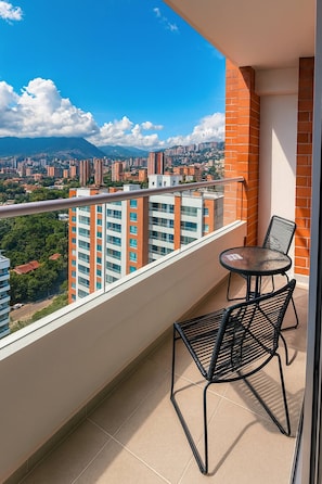 A balcony with a table and chairs, a view of a cityscape with buildings and mountains, and a clear blue sky. - Epic View 25 Pablo Tobón Cardiovascular (Medellín)