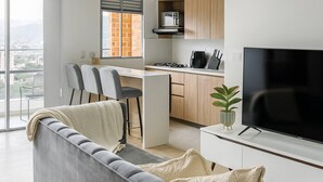 A modern living room with a grey sofa, a flat-screen TV, and a dining area with chairs and a kitchen in the background. - Epic View 25 Pablo Tobón Cardiovascular (Medellín)