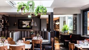 Um restaurante com cabines, mesas, plantas pendentes e um espaço de bar.