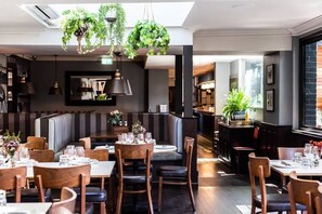 Un restaurante con cabinas, mesas, plantas colgantes y una zona de bar.