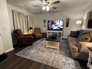 Ein Wohnzimmer mit Fernseher, einer Couch, einem Sessel, einem Couchtisch und einem Teppich mit Muster.