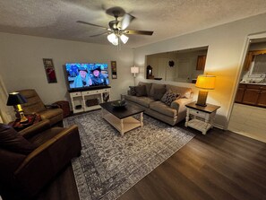 A living room with a television, a ceiling fan, a sofa, a coffee table, and a rug. - Spacious Jacksonville 3 Bedroom Home Near Jax State and Downtown (Jacksonville)