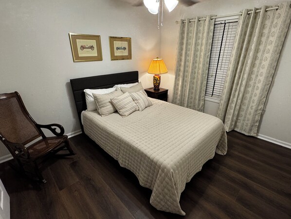 A bedroom with a bed, a chair, a nightstand with a lamp, and two framed pictures on the wall. - Spacious Jacksonville 3 Bedroom Home Near Jax State and Downtown (Jacksonville)