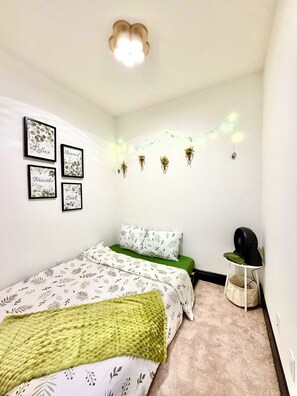 Een slaapkamer met een bed, een groen kussen, een nachtkastje met een speaker, en wandlampen.