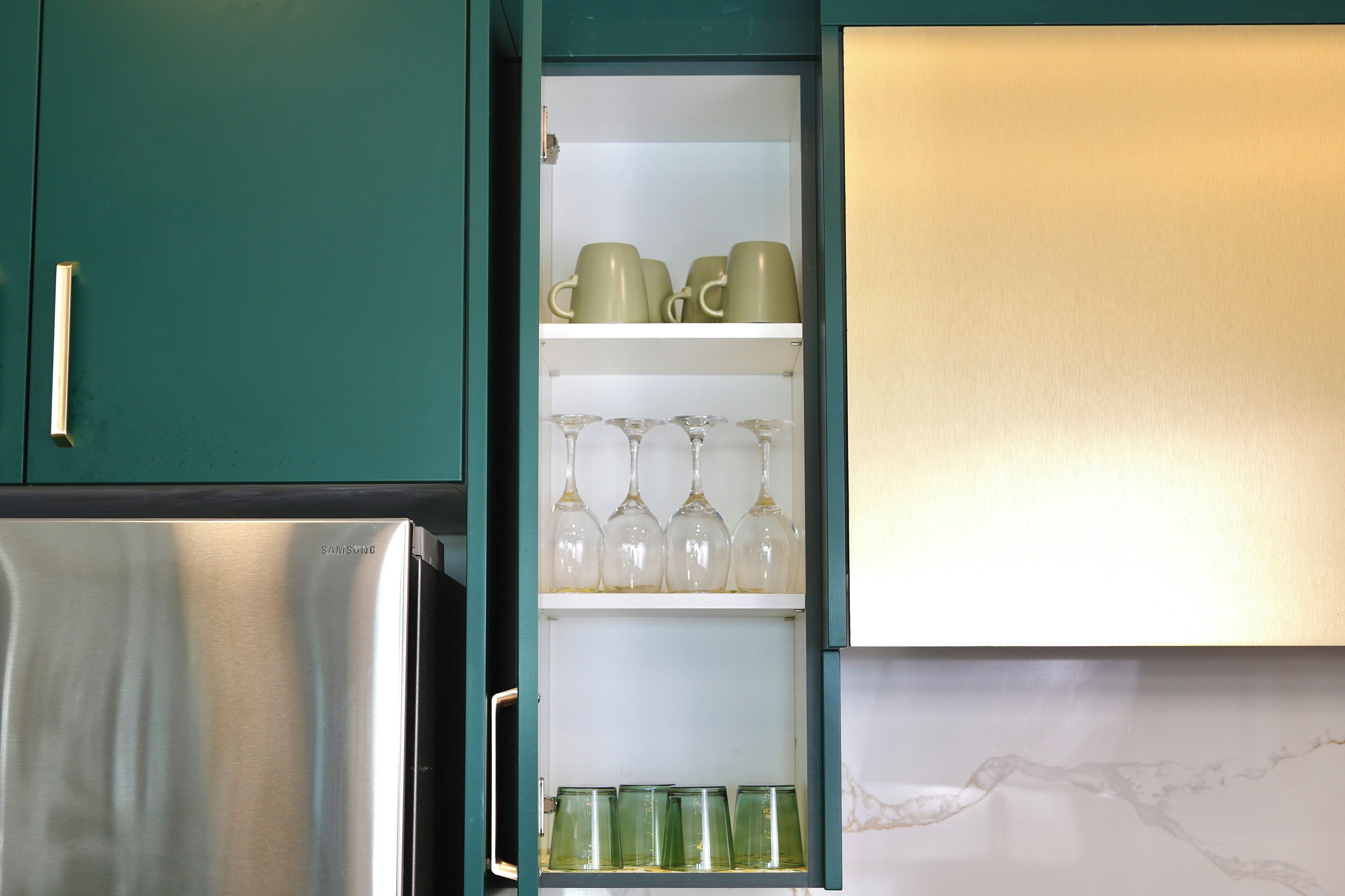 A kitchen with teal cabinets, a stainless steel refrigerator, and a shelf with glassware and green cups.