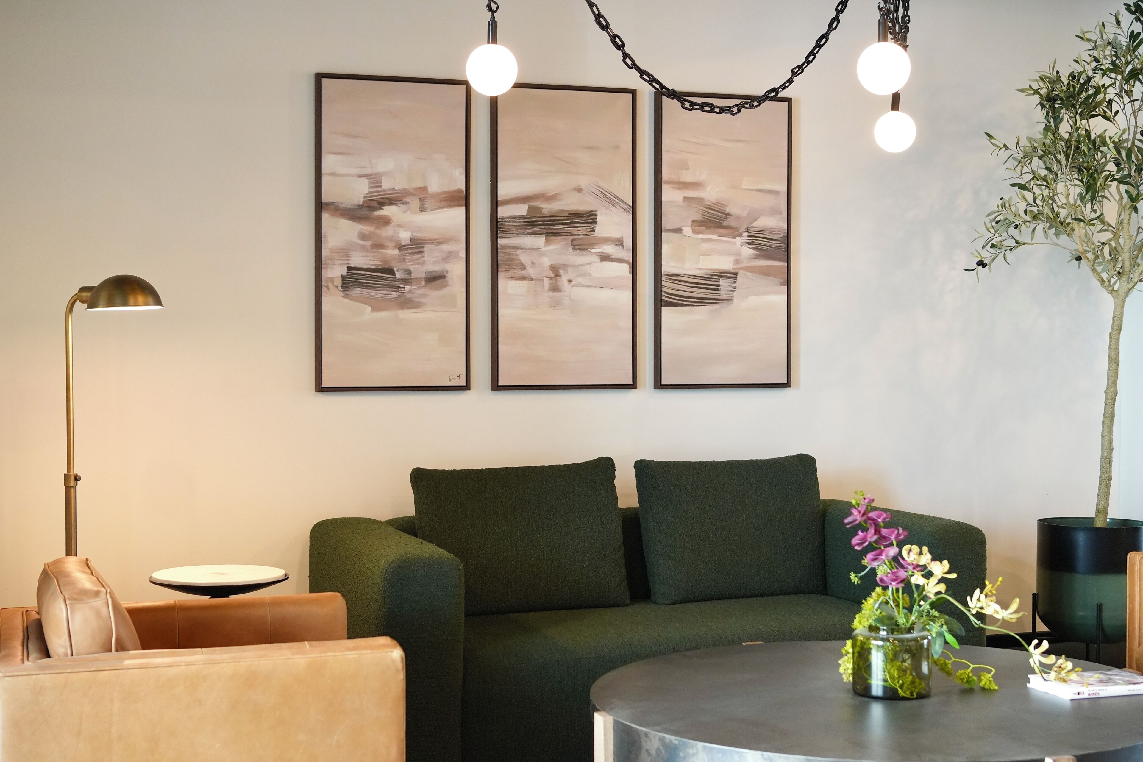Un salón con un sofá verde, una mesa de centro redonda con un jarrón de flores, una lámpara de pie y arte abstracto en la pared.