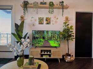 A living room with a TV, a bookshelf, a plant, and a door. - Green Lux Garden - 2BR 1Bath - Free Parking (Calgary)