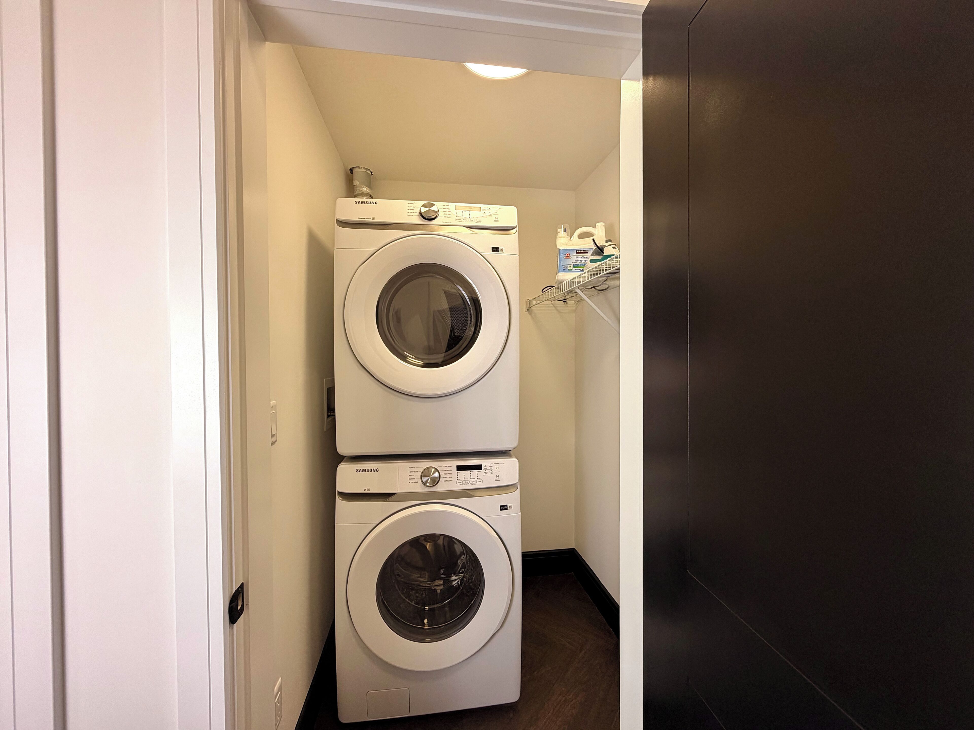 Un cuarto de lavandería con dos lavadoras apiladas y un estante con productos de limpieza.
