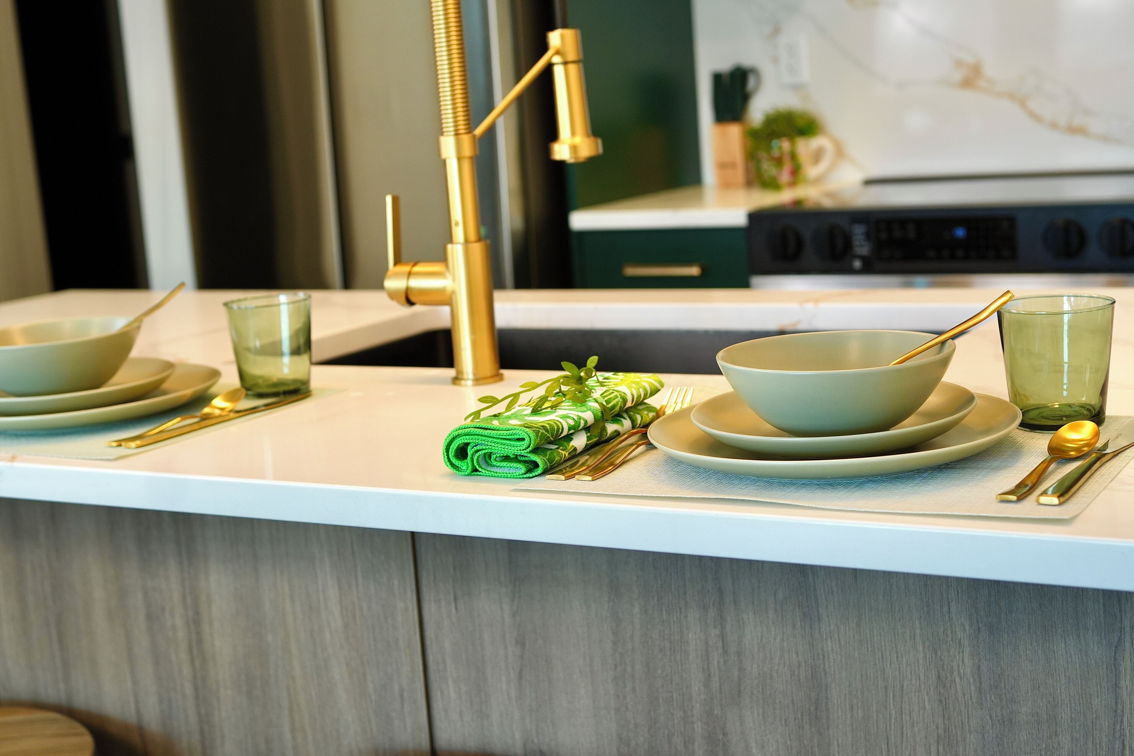 A kitchen counter with a modern faucet, a bowl, a glass, and a green towel.