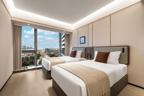 A hotel room with two beds, a large window with a city view, and a flat-screen TV on the wall.