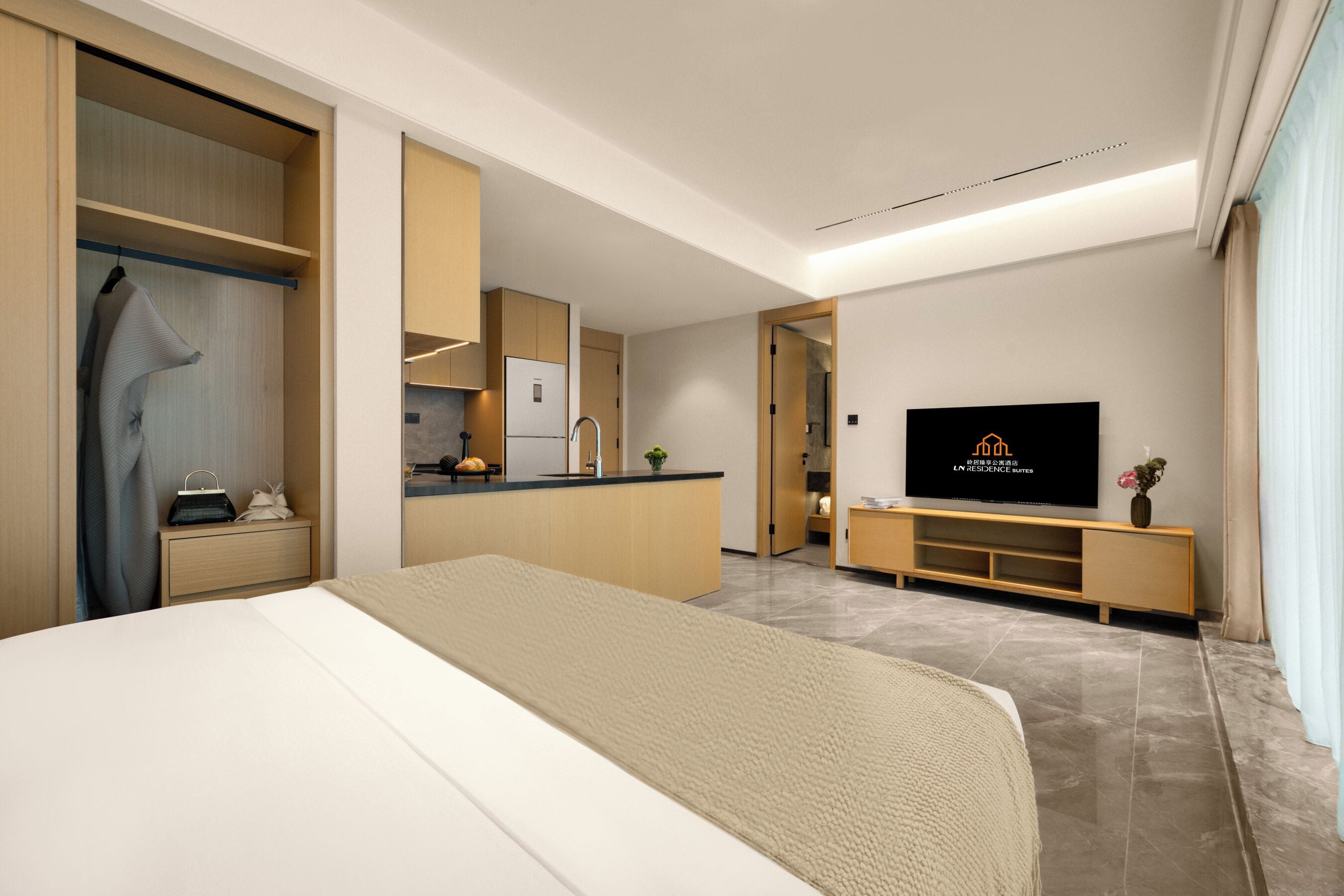 A modern hotel room with a bed, a TV, a kitchenette, and a walk-in closet.