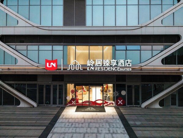 A modern hotel entrance with a prominent logo, a sign indicating it's a residence hotel, and a staircase leading to the entrance.