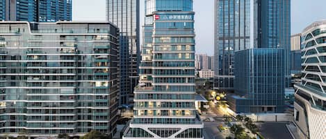 A modern hotel with a curved glass facade, surrounded by high-rise buildings.