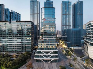 A modern hotel with a curved glass facade, surrounded by high-rise buildings. - LN Residence suites (Guangzhou)