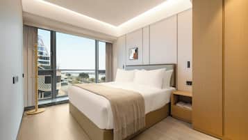 Habitación de hotel moderna con una cama grande, un armario de madera y vistas a un paisaje urbano a través de un ventanal amplio.