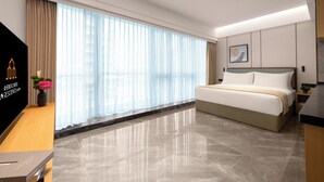 A hotel room with a bed, a desk, a TV, and a window with curtains. - LN Residence suites (Guangzhou)