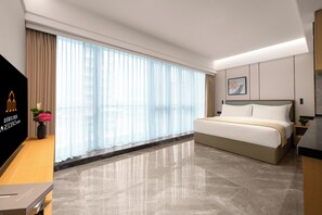 A hotel room with a bed, a desk, a TV, and a window with curtains. - LN Residence suites (Guangzhou)