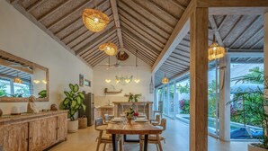 Un comedor amplio con una mesa y sillas de madera, un espejo grande y lámparas de mimbre colgantes.