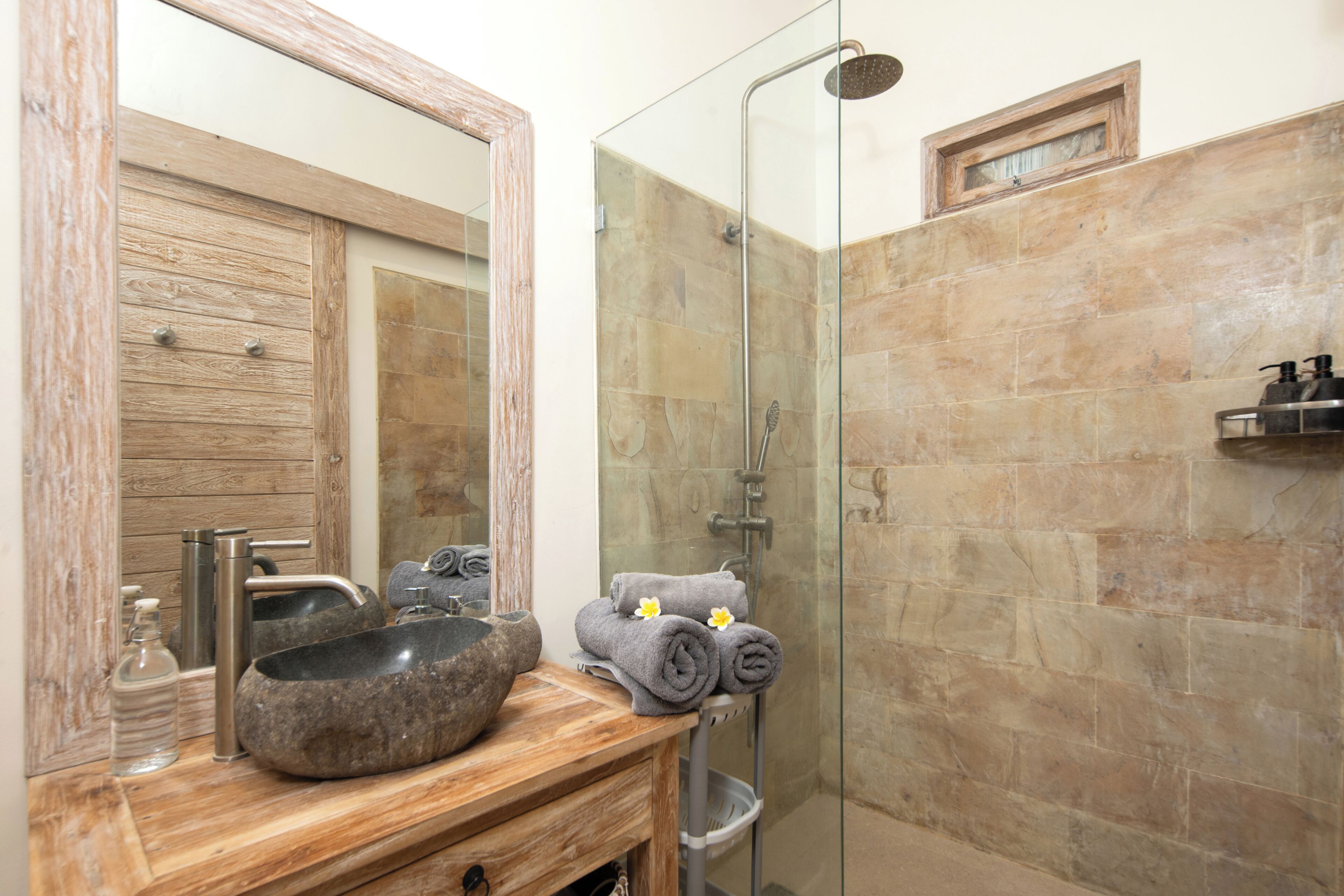 A bathroom with a wooden vanity, a stone sink, a glass shower enclosure, and a towel rack with towels.