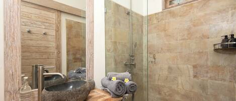 A bathroom with a wooden vanity, a stone sink, a glass shower enclosure, and a towel rack with towels.