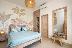 Un dormitorio con cama, lámparas de noche, armario, espejo y una pared con un mural floral.