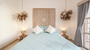 Un dormitorio con una cama grande, dos mesitas de noche, un cabecero decorativo y una ventana con cortinas.