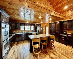 A wooden cabin interior with a kitchen, dining area, and a large window. - Glory on the Mountain (Bryson City)
