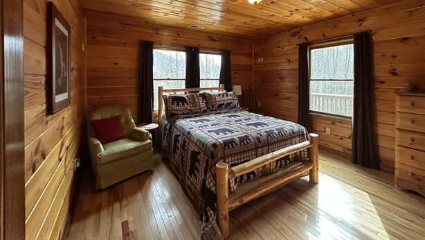 Ein Schlafzimmer einer Holzhütte mit einem Bett, einem Sessel und einem Fenster.