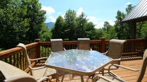 Eine Terrasse mit einem Tisch und Stühlen aus Glas, umgeben von einem Holgitter, mit Blick auf einen bewaldeten Bereich.
