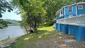 Una propiedad junto al río con una casa azul, cerca viva blanca y un espacio cubierto de césped.