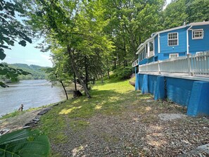 Ein Haus am Flussufer mit blauem Anstrich, weißem Zaun und einer Rasenfläche.