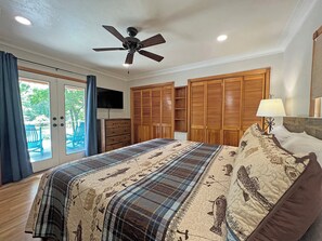 Ein Schlafzimmer mit einem Bett, einem Deckenventilator, einem Fernseher, Holzschränken und Blick ins Freie.