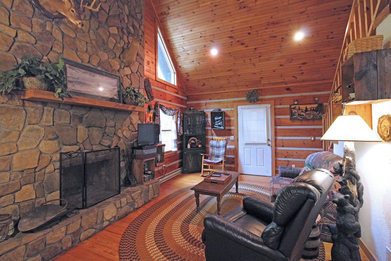 A log cabin interior with a stone fireplace, leather sofa, and a television.
