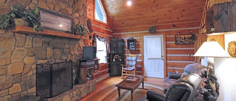 A log cabin interior with a stone fireplace, leather sofa, and a television.
