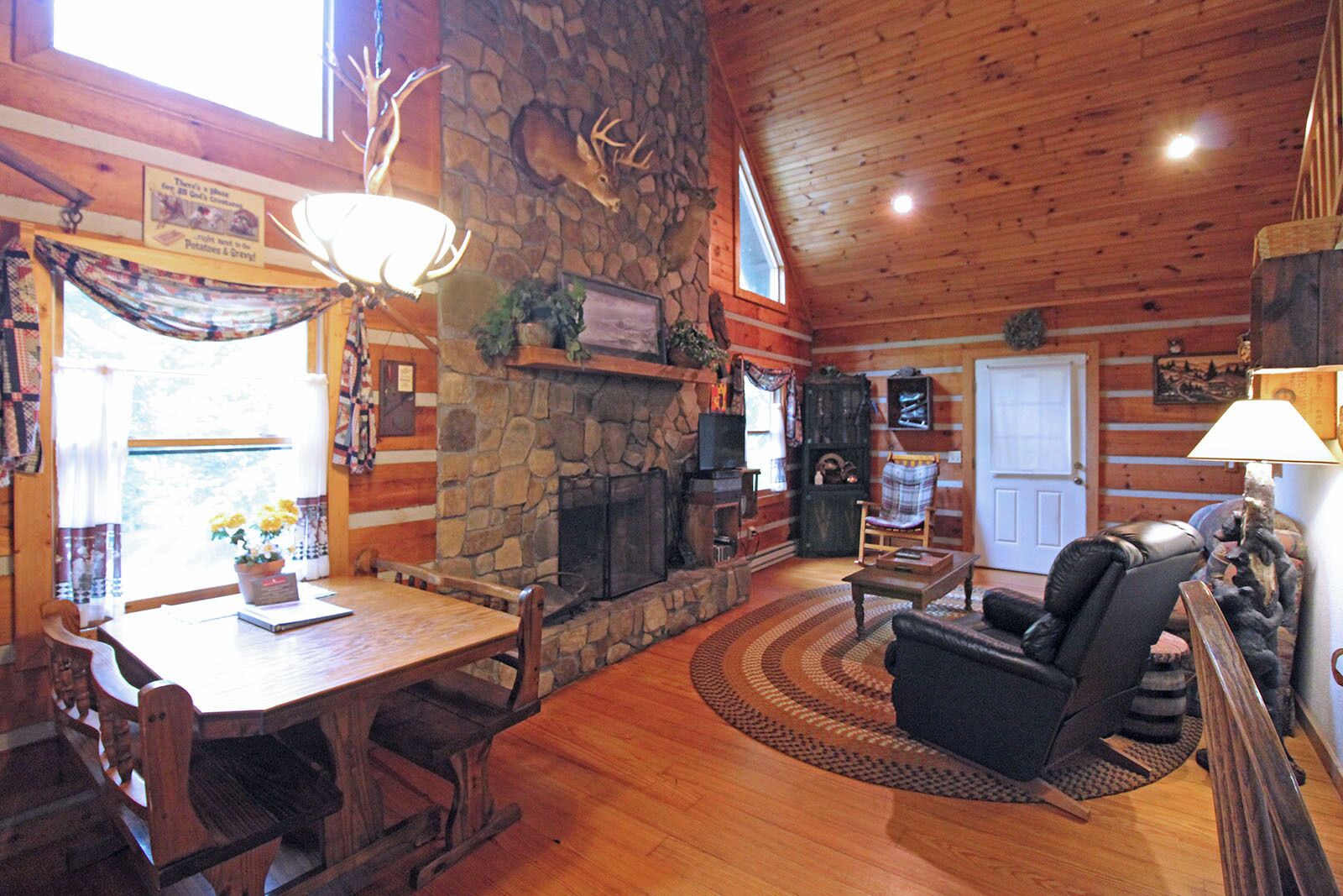 A log cabin interior with a stone fireplace, wooden furniture, and deer antlers on the wall.