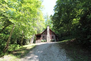 Une cabane dotée d’une cheminée en pierre, entourée d’une forêt dense.