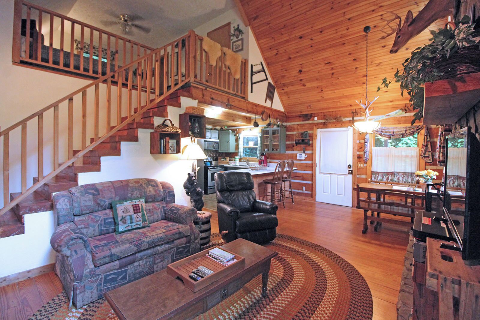 Ein geräumiges Wohnzimmer mit Holztreppe, Kamin, Essbereich und einer Küche im Hintergrund.