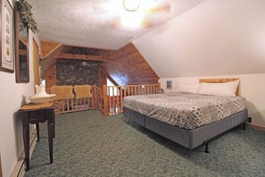 Une chambre avec un grand lit, un plafond en bois, un mur en pierre et un balcon doté d’une balustrade en bois.