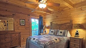 Een slaapkamer in een houten chalet, met een bed, nachtkastjes, een dressoir en een plafondventilator.