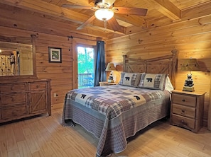 Ein Schlafzimmer in einer Holzhütte mit einem Bett, Nachttischen, einer Kommode und einem Deckenventilator.