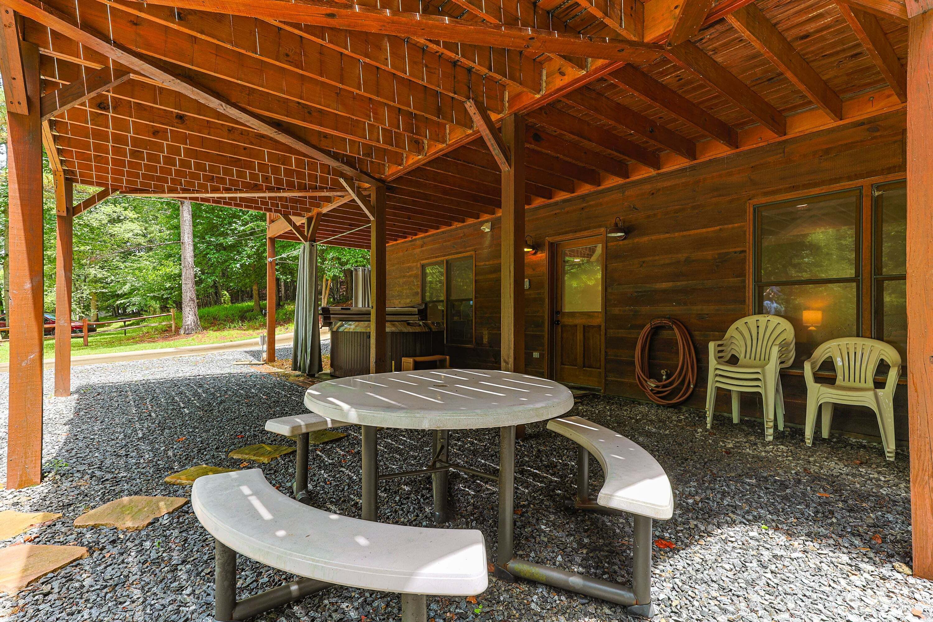 Un espace extérieur abrité, doté d’une table ronde et de bancs, le tout entouré d’une structure en bois.