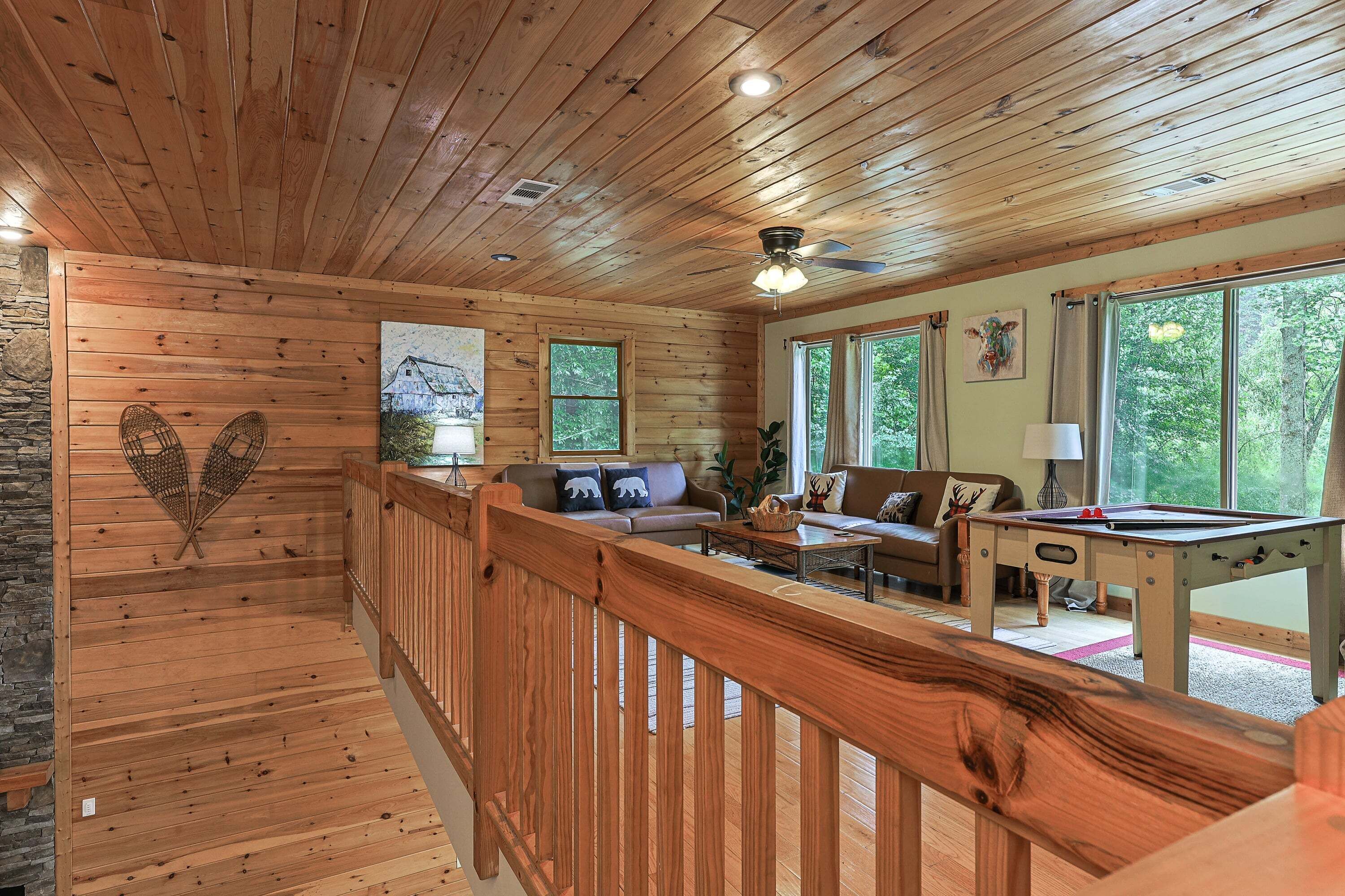 A wooden interior with a pool table, sofas, and a view of the outdoors.