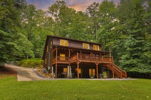 Een houten chalet met twee verdiepingen en een balkon, omgeven door een dicht bos.
