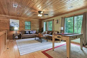 Een gezellig interieur van een blokhut met een bank, een salontafel, een pooltafel en grote ramen met uitzicht op het bos.