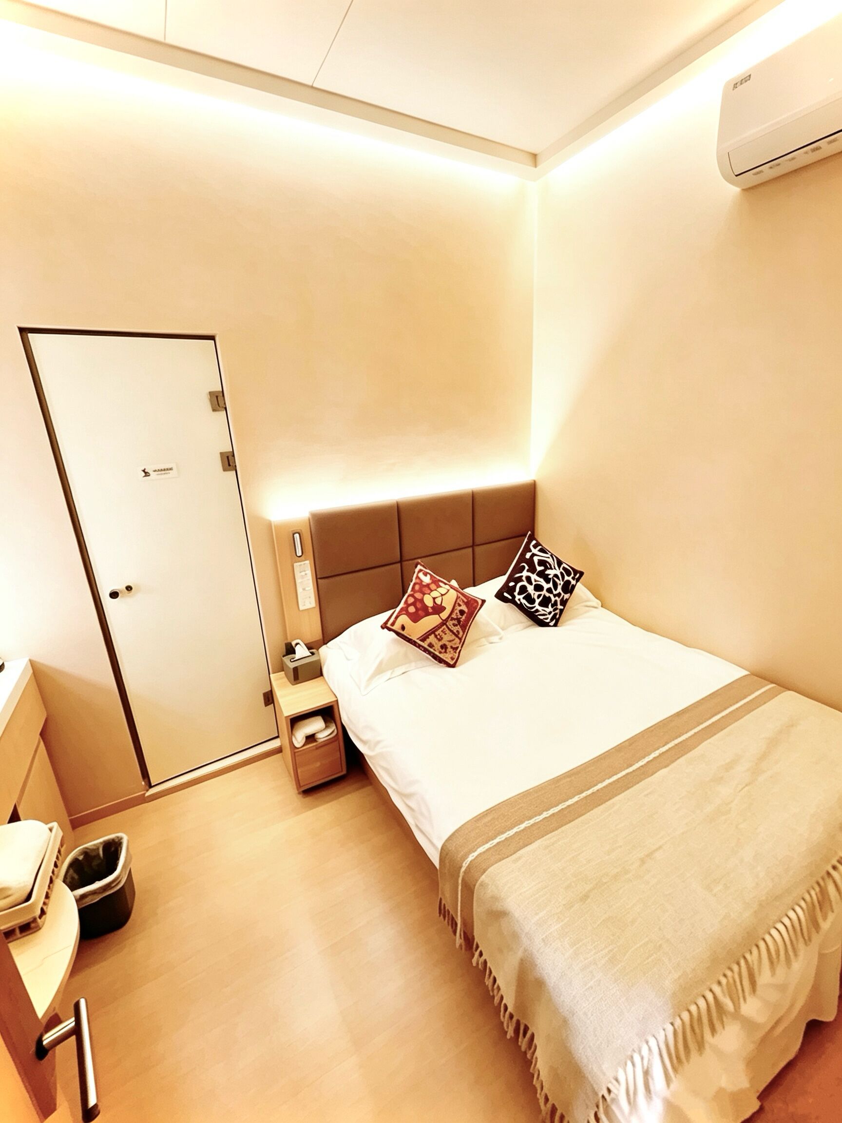 Una habitación de hotel con cama, mesita de noche y puerta.