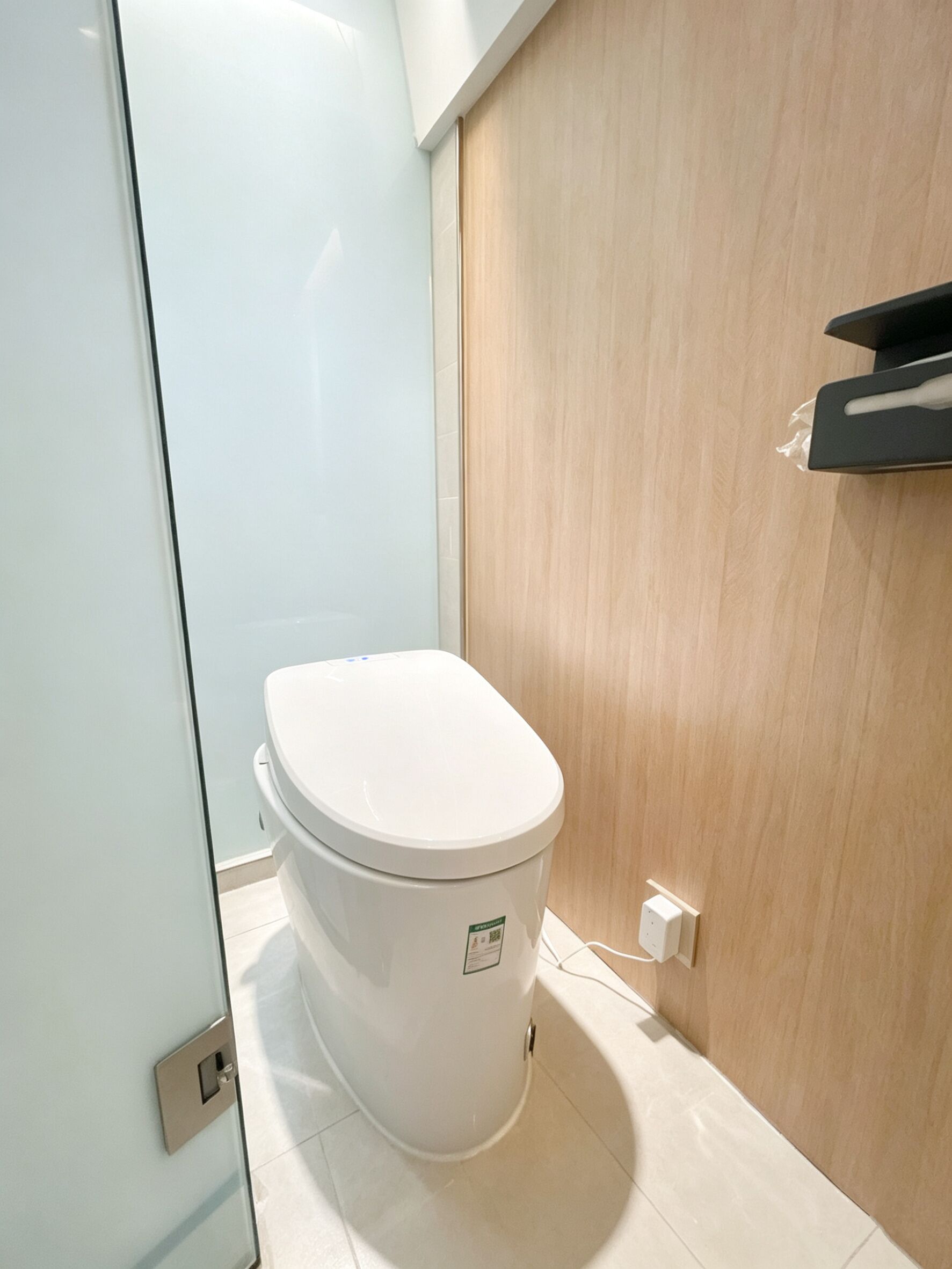 A modern bathroom with a white toilet, a wooden door, and a glass shower enclosure.