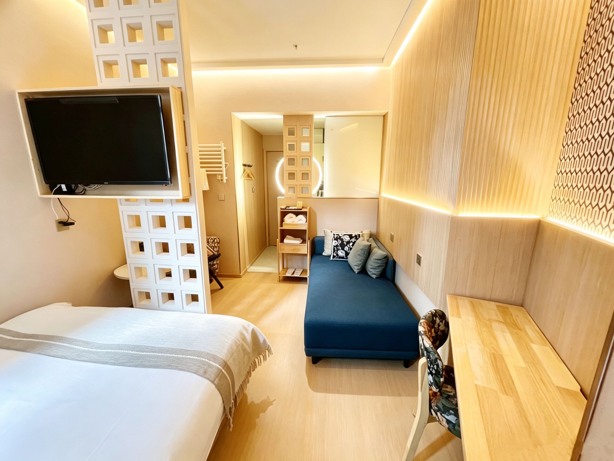 A modern hotel room with a large bed, a blue sofa, a TV, and a wooden headboard.