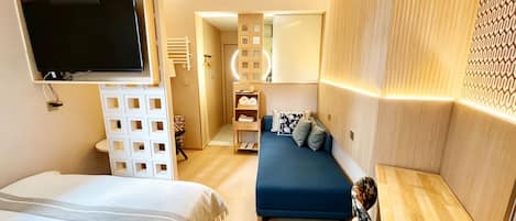A modern hotel room with a large bed, a blue sofa, a TV, and a wooden headboard.
